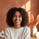 A smiling young woman looking at the camera, conveying happiness and trust. The background is blurred with warm tones.