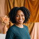 A diverse woman with healthy, glowing skin smiling in a warm, professionally lit studio environment.